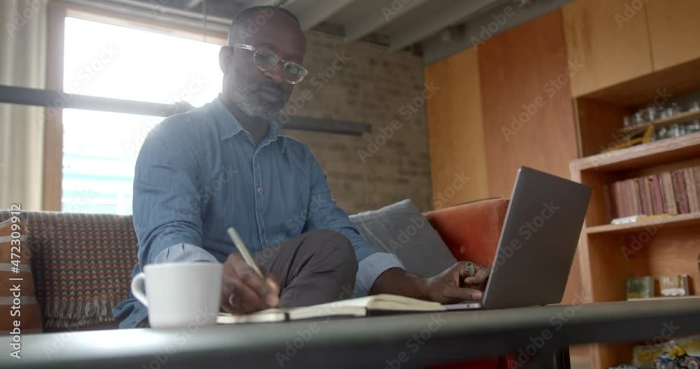 Black Male working at home on sofa using laptop in living room Black Male working at home on sofa using laptop in living room
