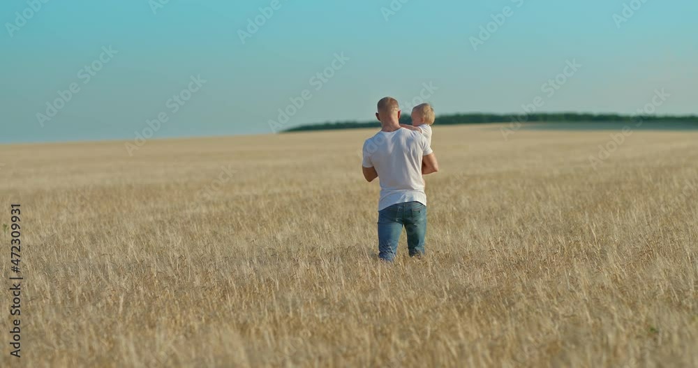 Father and child are walking across the field, dad is holding the baby in his arms. Happy fatherhood and childhood, the father spends time with the child, a walk. View from the back. 4k, ProRes Father and child are walking across the field, dad is holding the baby in his arms. Happy fatherhood and childhood, the father spends time with the child, a walk. View from the back. 4k, ProRes