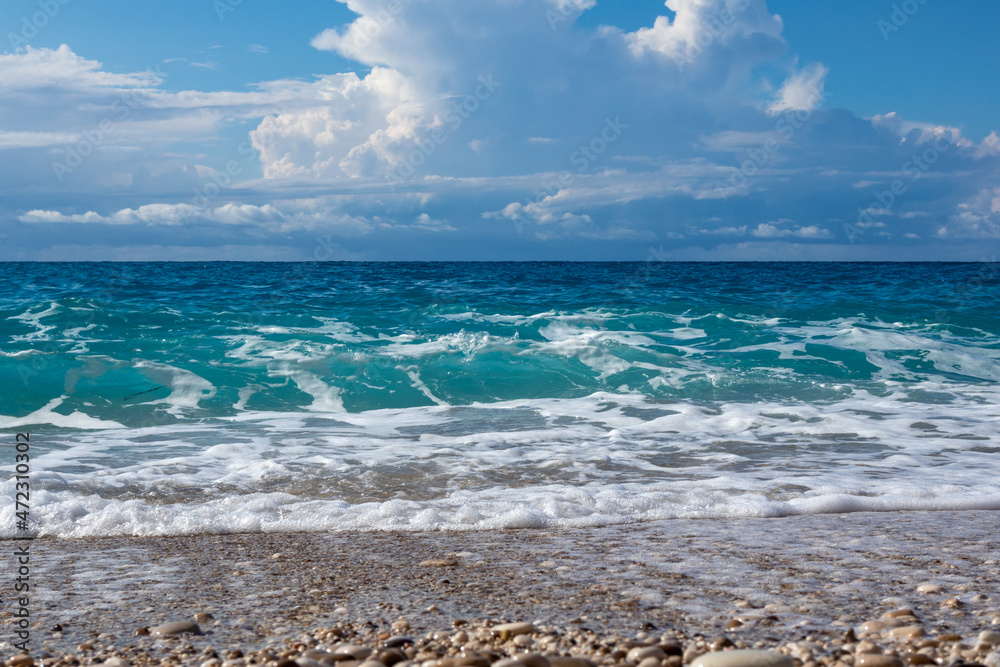 Scenic white foam on pebble beach with blue stormy waves and epic cloudscape on coast of Lefkada island in Greece. Summer nature travel to Ionian Sea Scenic white foam on pebble beach with blue stormy waves and epic cloudscape on coast of Lefkada island in Greece. Summer nature travel to Ionian Sea