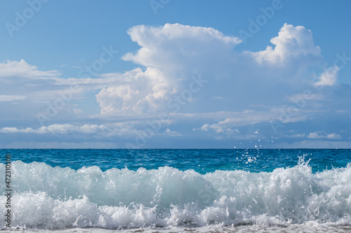 Shining waves splash with white foam on pebble beach. Blue sea and epic clouds on coast of Lefkada island in Greece. Summer travel to Ionian Sea