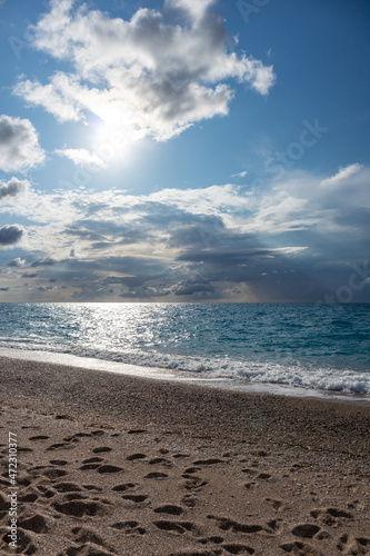 Fototapeta Naklejka Na Ścianę i Meble -  Sun and clouds above Mylos beach shore on sunny coast with blue seascape. Lefkada island in Greece. Summer travel to Ionian Sea. Vertical