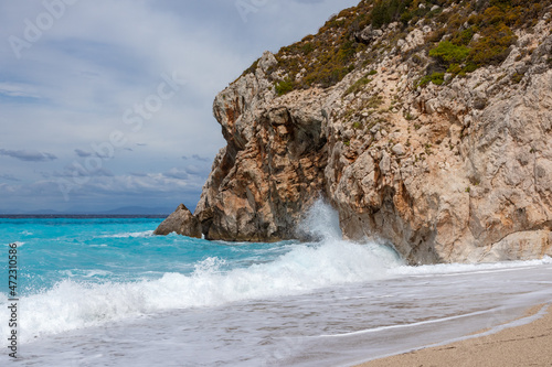 Azure vibrant stormy waves with white foam breaking rocky coast. Mylos sandy beach with epic cloudy sky on Lefkada island in Greece. Summer travel to Ionian Sea photo