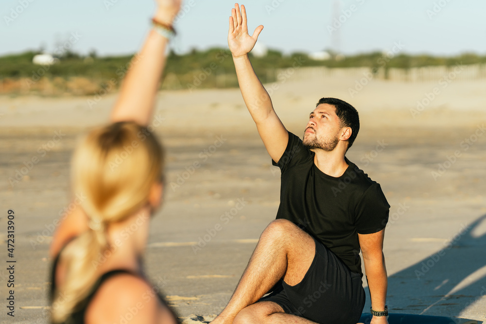 Obraz premium Man raisin arm while doing a yoga next to his coach on the beach