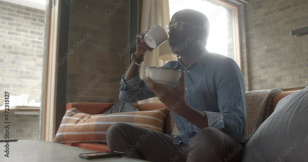 Black Male having breakfast at home on sofa and checking smart phone Black Male having breakfast at home on sofa and checking smart phone