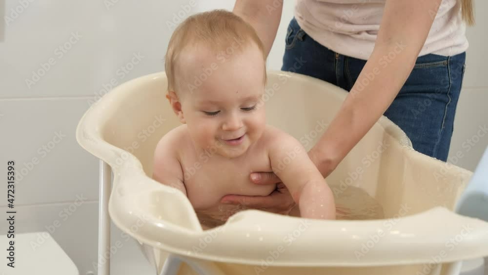 Cheerful smiling baby boy splashing water and playing while having bath with mother. Concept of children hygiene, healthcare and parenting. Cheerful smiling baby boy splashing water and playing while having bath with mother. Concept of children hygiene, healthcare and parenting.
