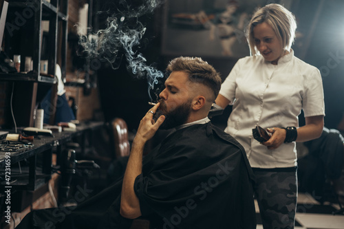 Young bearded man getting haircut by hairdresser and smoking a cigarette © Zamrznuti tonovi