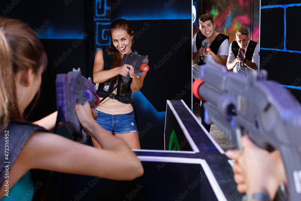 Two happy cheerful positive laser tag teams playing enthusiastically and aiming at each other in dark room