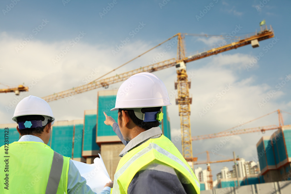 rear view foreman construction discussing at the site pointing at the crane in the background rear view foreman construction discussing at the site pointing at the crane in the background