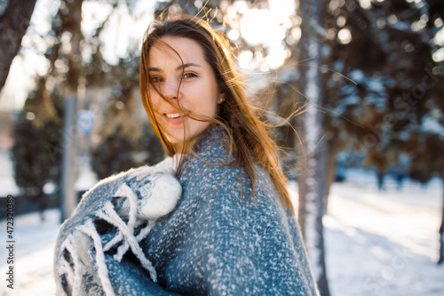 Close-up portrait of happy girl in woolen sweater enjoying winter moments. Outdoor photo of a girl with red hair wearing a blue scarf and mittens. Snowy winter park.