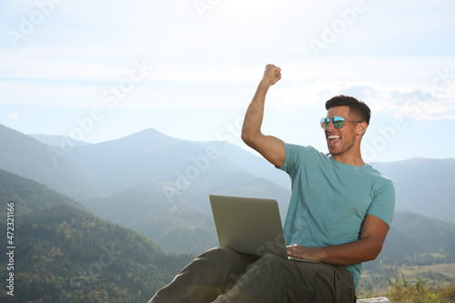 Man working with laptop in mountains on sunny day © New Africa