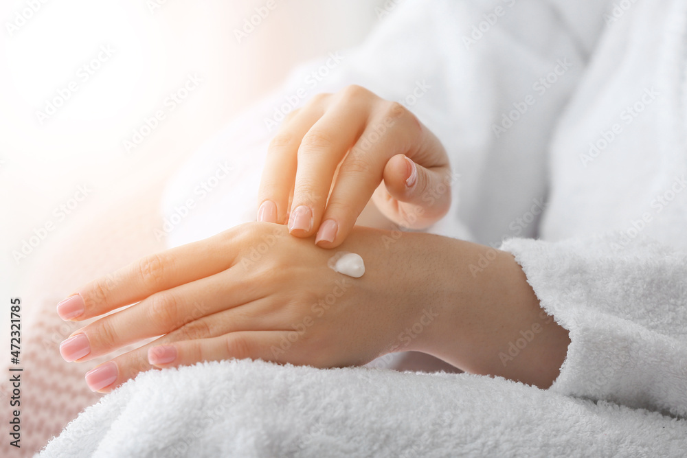 Young woman applying cosmetic cream onto her hands at home, closeup