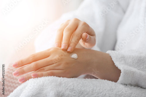 Young woman applying cosmetic cream onto her hands at home  closeup