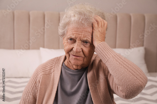 Senior woman with headache in bedroom at home