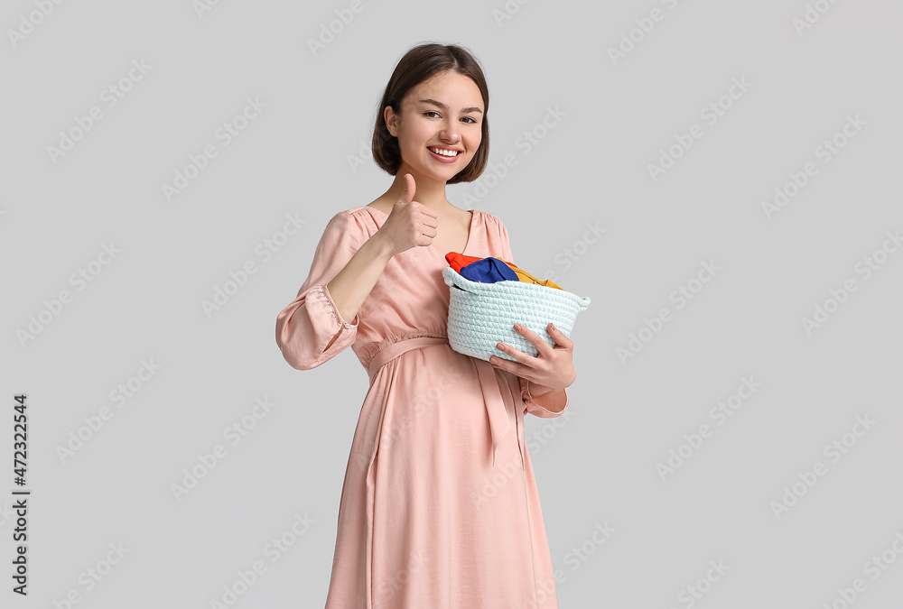 Young pregnant woman holding basket with baby clothes on light background Young pregnant woman holding basket with baby clothes on light background