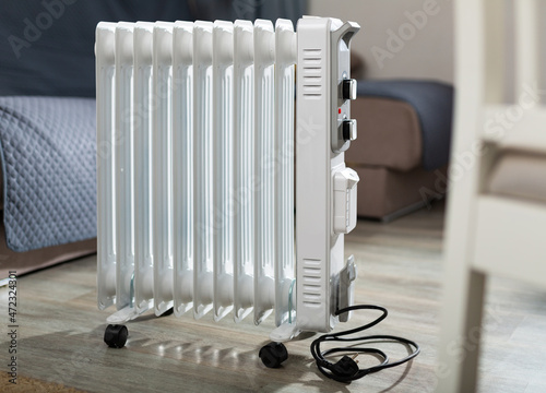 White metal portable oil heater standing in home room. Electric appliance for heating house..