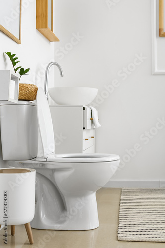White toilet bowl and chest of drawers near light wall in restroom © Pixel-Shot