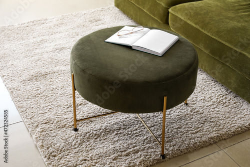 Open book with eyeglasses on green pouf in living room