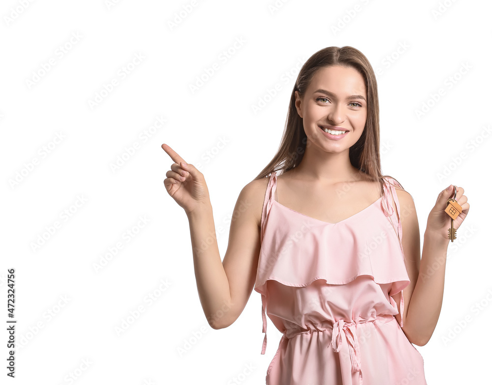 Smiling young woman with key from house pointing at something on white background Smiling young woman with key from house pointing at something on white background
