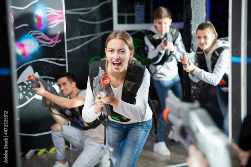 Emotional girl with laser pistol playing laser tag with friends on dark labyrinth..