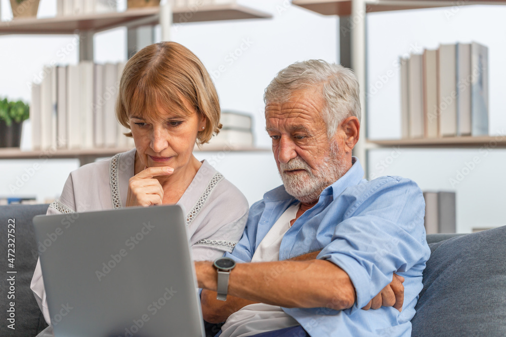 Worried senior couple checking their bills and work on netbook read document information at home, retired elderly old family reading documents with laptop