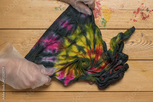 The process of unfolding a T-shirt painted in tie dye style. Flat lay. © kvladimirv
