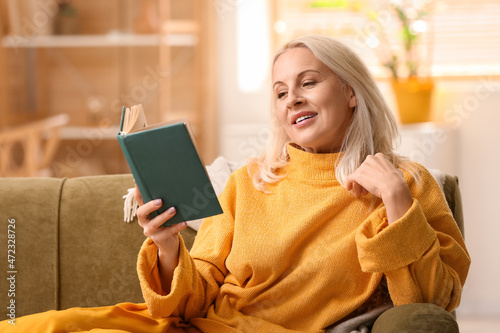 Beautiful mature woman reading book at home on autumn day photo