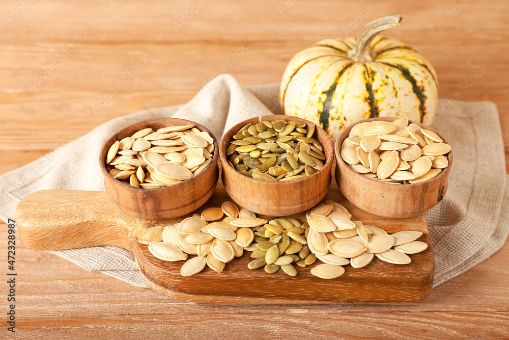 Bowls with natural pumpkin seeds on wooden background