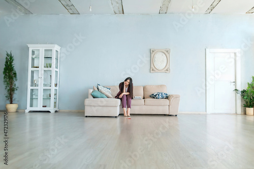 a woman is sad on the couch in a large apartment. long-range plan © Lema-lisa
