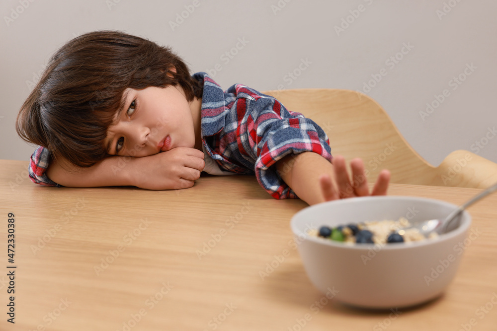 Cute little boy refusing to eat his breakfast at table on grey background Cute little boy refusing to eat his breakfast at table on grey background