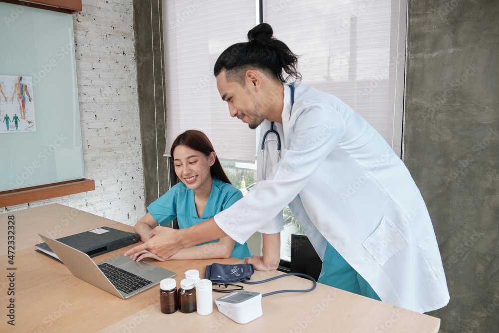 Healthcare team partners. Two uniformed young Asian ethnicity doctors are co-workers discussing medication in hospital's clinic office. Specialist persons are experts and professionals. Healthcare team partners. Two uniformed young Asian ethnicity doctors are co-workers discussing medication in hospital's clinic office. Specialist persons are experts and professionals.