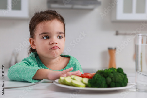 Cute little girl refusing to eat vegetables in kitchen