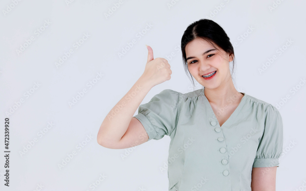 Portrait close up studio shot of Asian young teen scowl frown moody female model with ponytail hairstyle wearing casual outfit standing holding hand showing approval thumb up on white background Portrait close up studio shot of Asian young teen scowl frown moody female model with ponytail hairstyle wearing casual outfit standing holding hand showing approval thumb up on white background