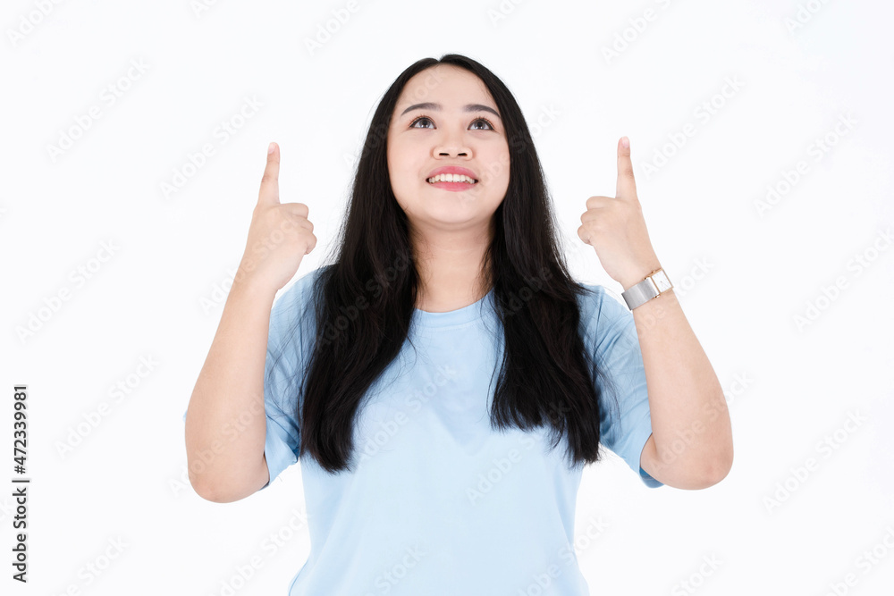 Portrait closeup studio shot of Asian young chubby plump long black hair female model in blue casual t shirt and wrist watch holding hands pointing up presenting smiling look up on white background Portrait closeup studio shot of Asian young chubby plump long black hair female model in blue casual t shirt and wrist watch holding hands pointing up presenting smiling look up on white background