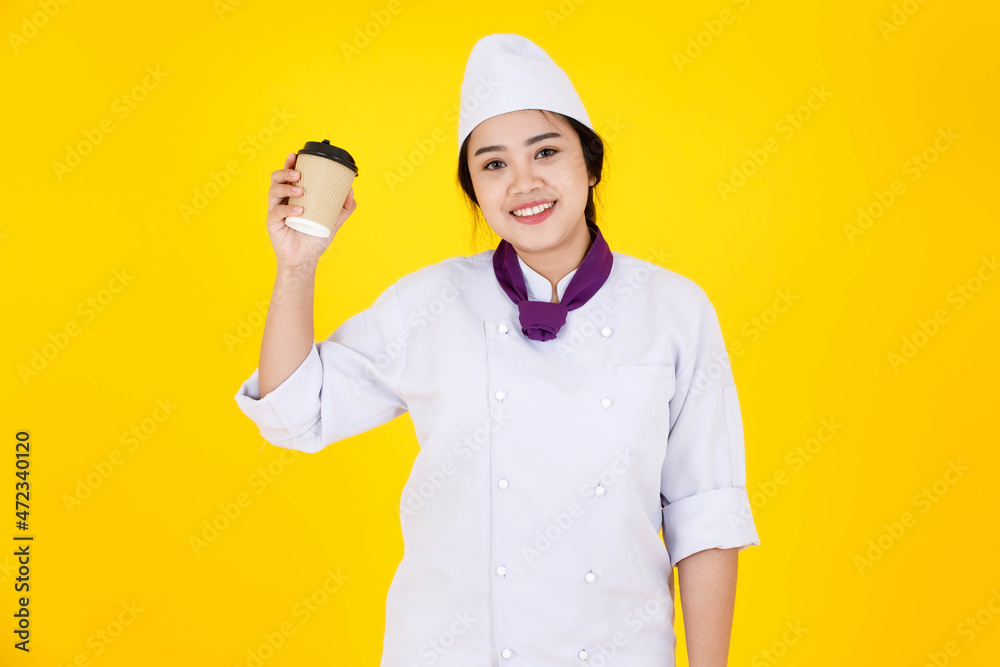 Portrait studio shot of Asian professional successful hotel restaurant female executive chef in white cooking uniform with hat scarf stand smiling holding disposable coffee cup on yellow background