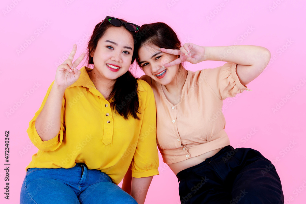 Portrait closeup studio shot of two Asian young cheerful friends or sisters in casual outfit with braces and eyeglasses smiling and pose funny action together on pink background Portrait closeup studio shot of two Asian young cheerful friends or sisters in casual outfit with braces and eyeglasses smiling and pose funny action together on pink background