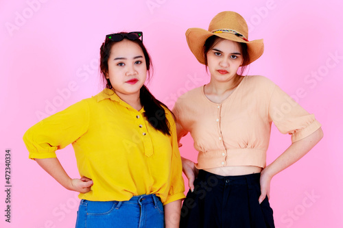 Portrait closeup studio shot of two Asian young cheerful friends or sisters in casual outfit with braces and eyeglasses smiling and pose funny action together on pink background