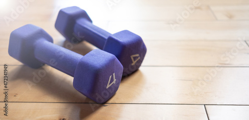 Two small purple dumbbells laying on a hardwood floor inside a gym 