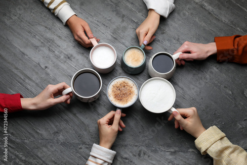 People holding different cups with aromatic hot coffee at grey table, top view