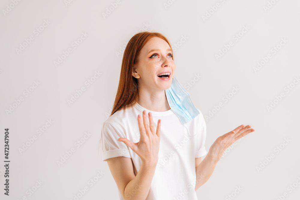 Studio portrait of happy cheerful young woman in casual t-shirt taking off disposable protective face mask, standing on white isolated background. Flu epidemic, dust allergy, protection against virus Studio portrait of happy cheerful young woman in casual t-shirt taking off disposable protective face mask, standing on white isolated background. Flu epidemic, dust allergy, protection against virus