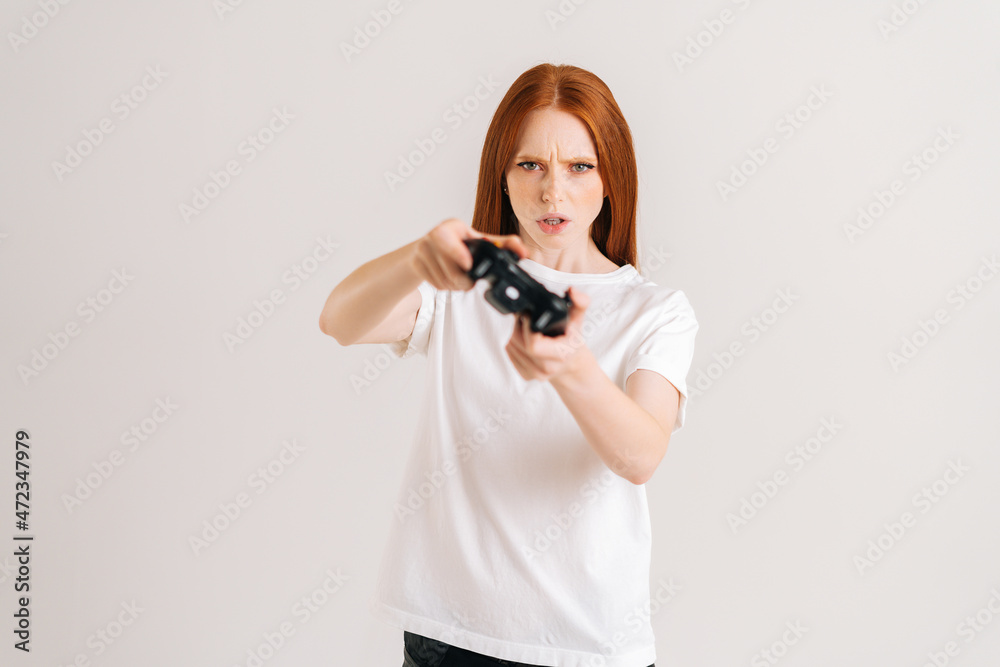 Studio portrait of serious young woman playing video game with controller looking at camera on white isolated background. Happy lady using joystick on console enjoying online game.
