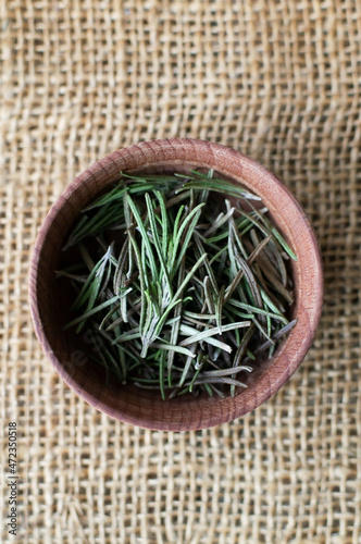 Dry rosemary in a wooden bowl on the table. Rustic style. Top view. The dry spice is added to meat, salads, soups or drinks. Ingredient for the bouquet Garni, Provencal herbs and Italian herbs.