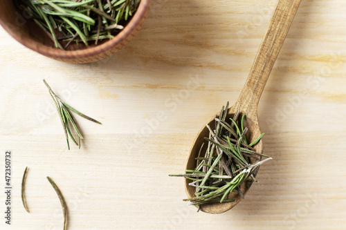 Dry rosemary in a wooden bowl with a spoon and a few sprigs on a wooden table. Rustic style. The spice is added to meat, salads, soups or drinks. An ingredient for a bouquet Garni. Top view