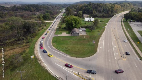 Corvette car parade through rural roads in Wisconsin. Cars turning onto highway. Residential home and garage on corner. Multiple directional signs present. 