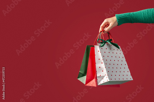 Christmas shopping online. Christmas shopping bags, gift boxes and a hand with a phone on a red background.