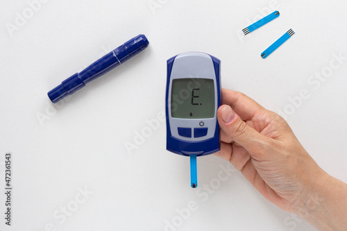Top view of woman hand holding glucose meter with letter E on monitor means error on the white background photo
