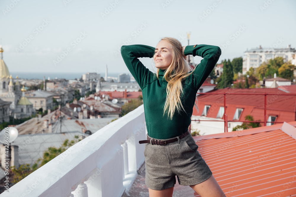 beautiful blonde woman looks at the city from the roof of the house