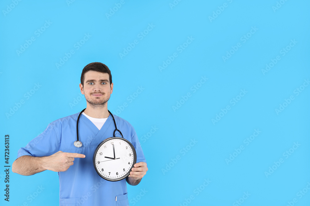 Male nurse with clock on blue background Male nurse with clock on blue background