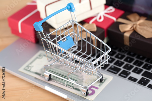 Shopping cart with banknotes on the computer and gifts