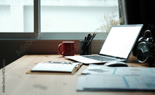 Laptop computer with blank screen  coffee cup  clipboard and pencil holder on wooden desk.