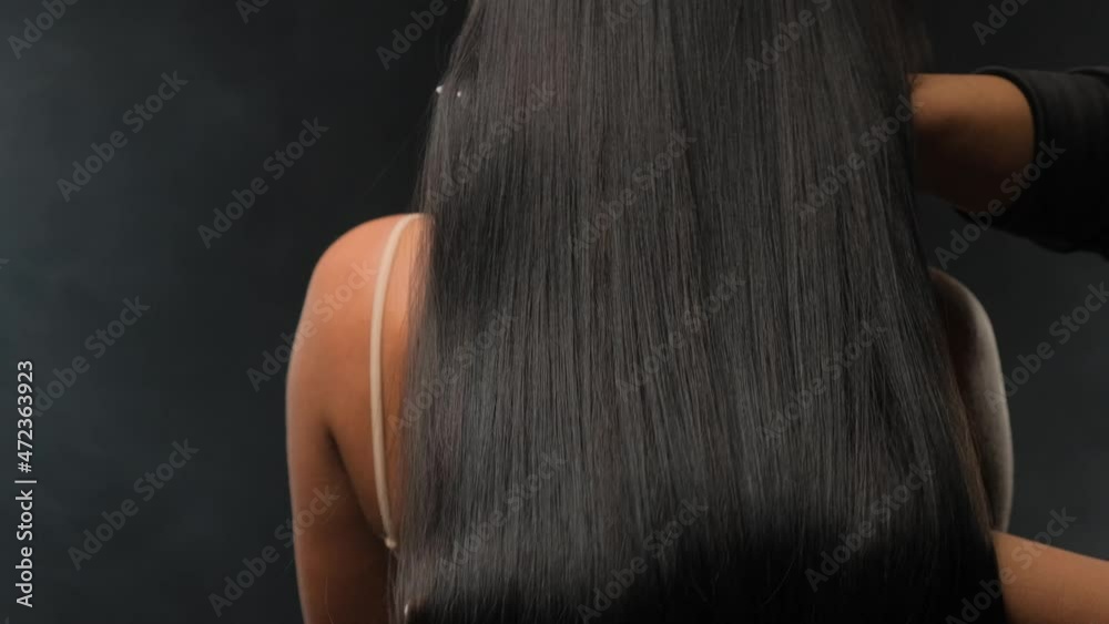 Close-up of a brunette with luxurious hair on a dark background. The girl stands with her back and develops her hair.